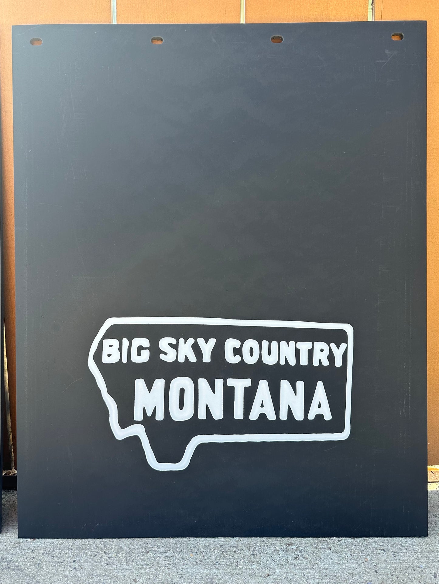 Black mudflaps with 'Big Sky Country Montana' text on a wooden background