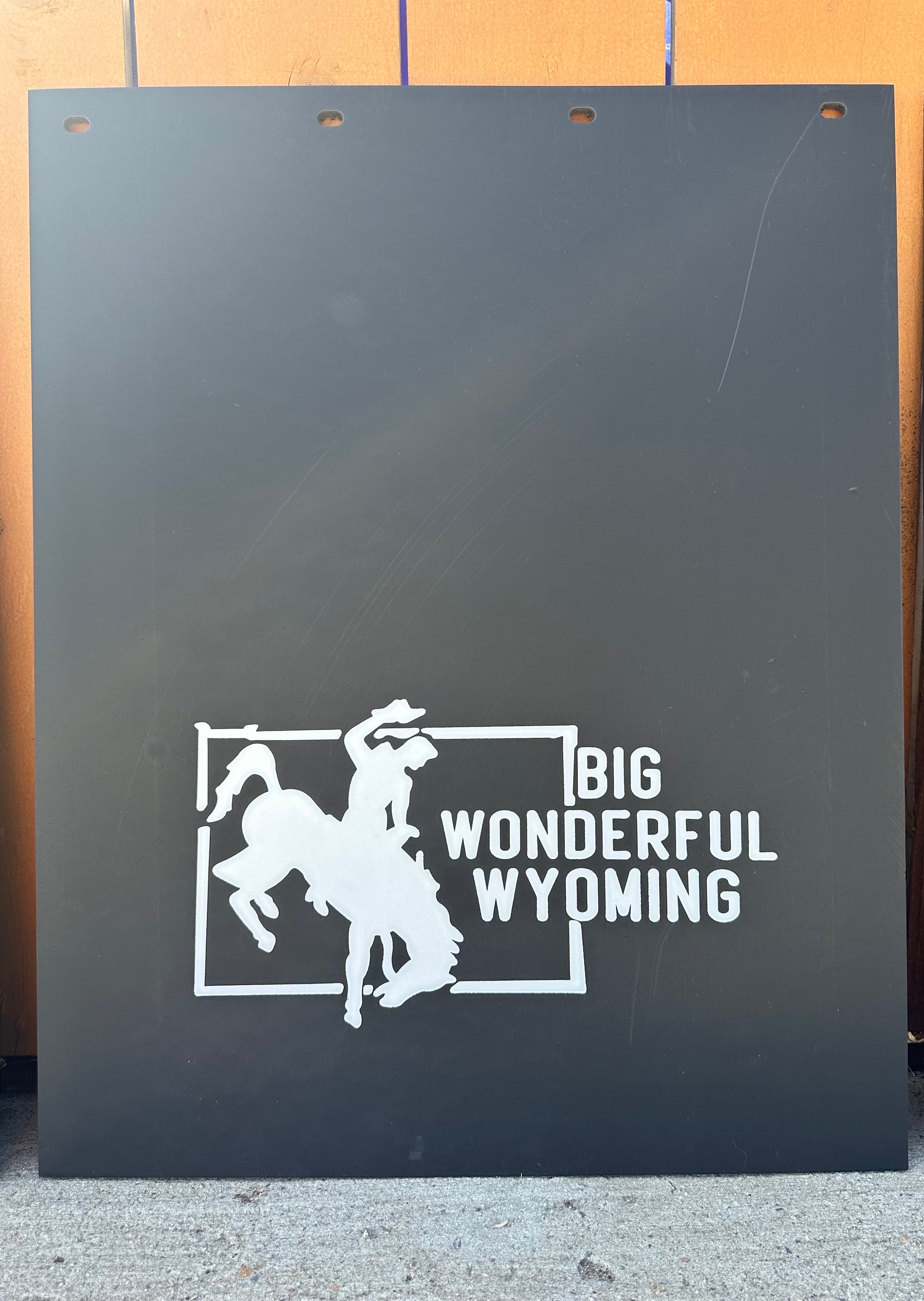 Black mudflaps with white graphic and text 'Big Wonderful Wyoming' on a wooden background
