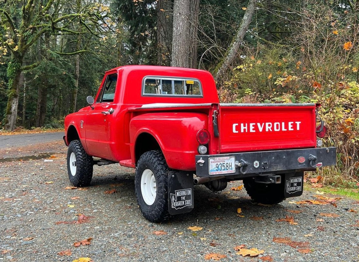 Red Chevrolet truck with retro Washington mudflaps parked on a road with trees in the background