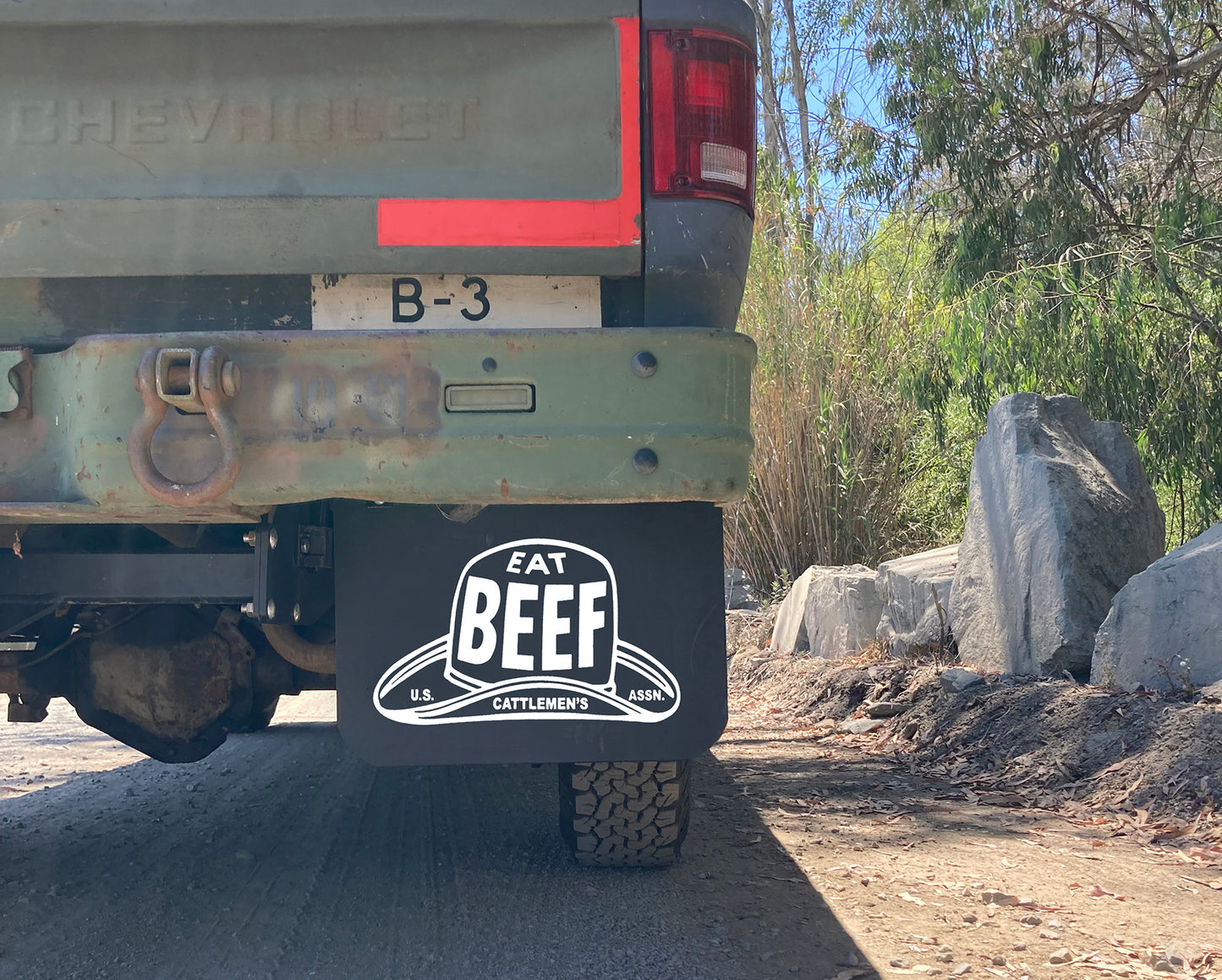 Back of a Chevrolet truck with a 'Eat Beef' mudflap in a natural setting.