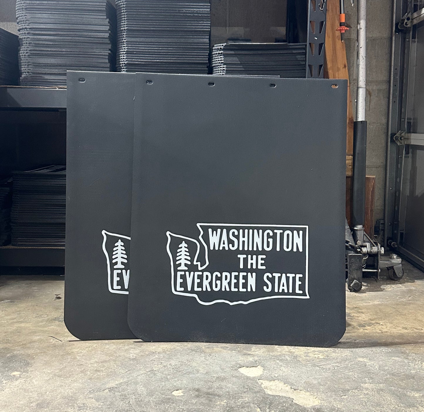 Two black mudflaps with 'Washington The Evergreen State' text and logo in a garage