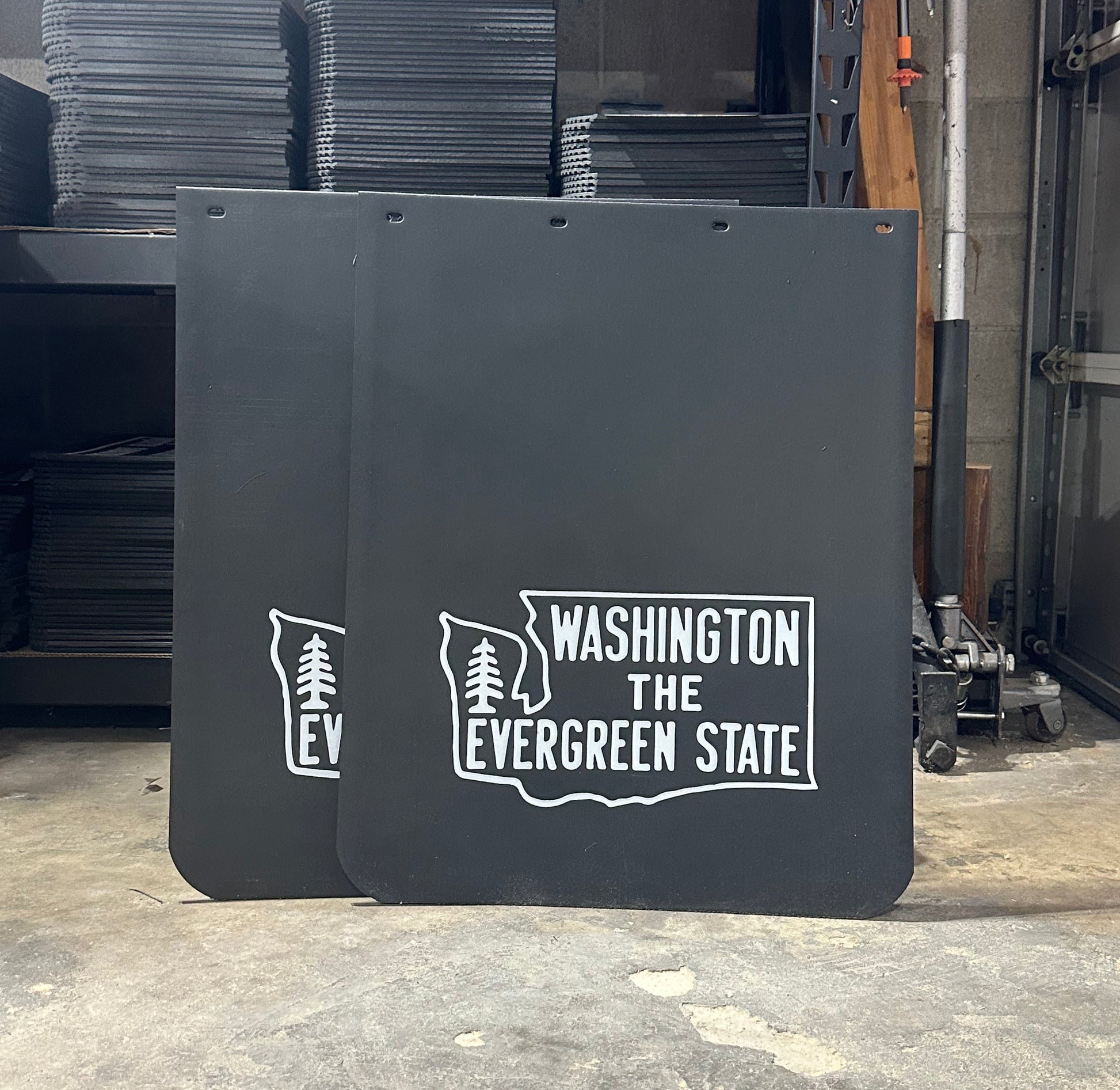 Two black mudflaps with 'Washington The Evergreen State' text and logo in a garage
